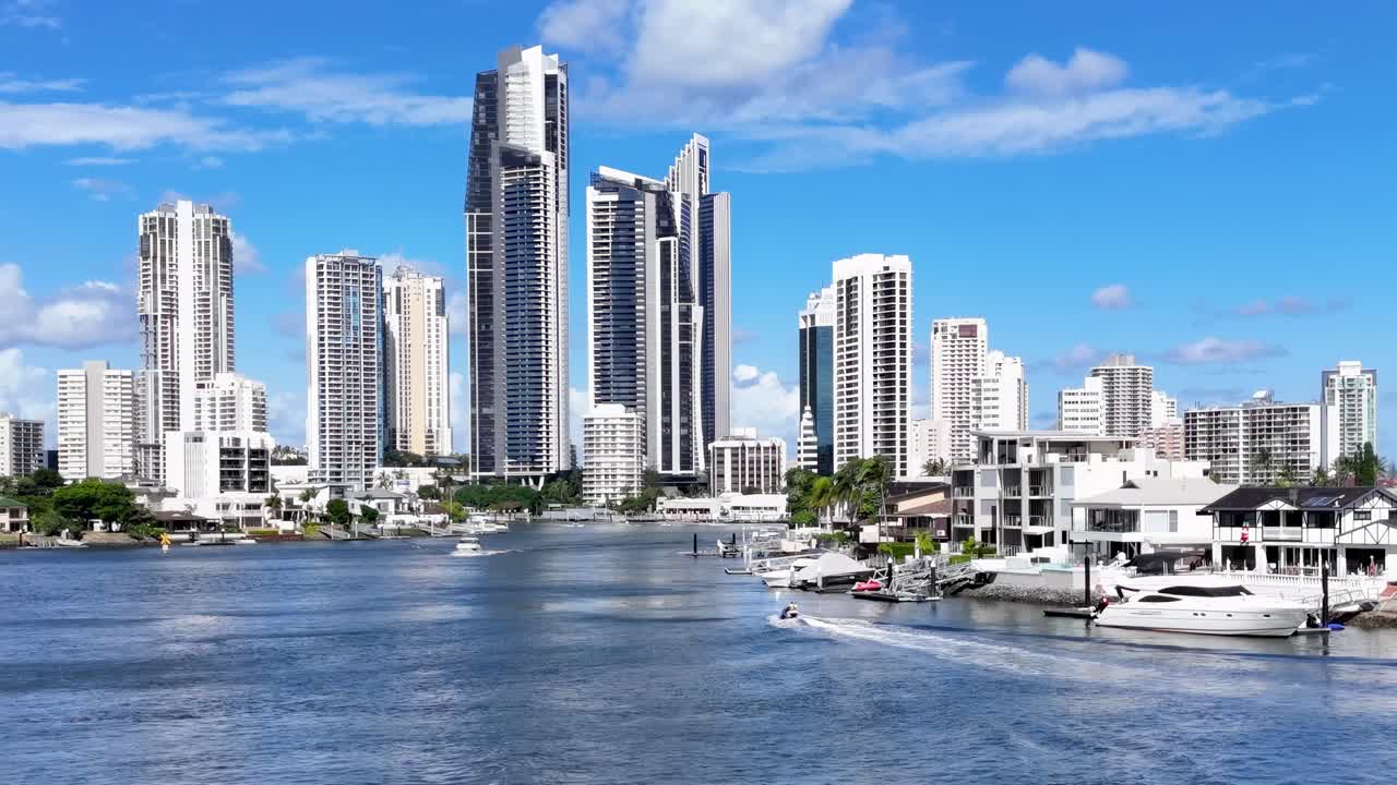 A vibrant city skyline with boats along a sunny waterfront, showcasing modern architecture and clear blue skies.
