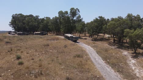 Israel-Army-infantry-squad-soldiers-on-vehicle-driving-through-green-field-at-training-ground-country-road,-Aerial-Tracking-shot