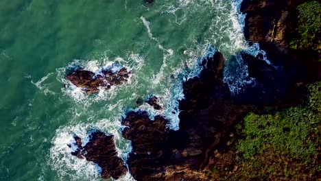 Aerial-shot-flying-over-sunlit-waves-crashing-against-rocky-California-cliffs