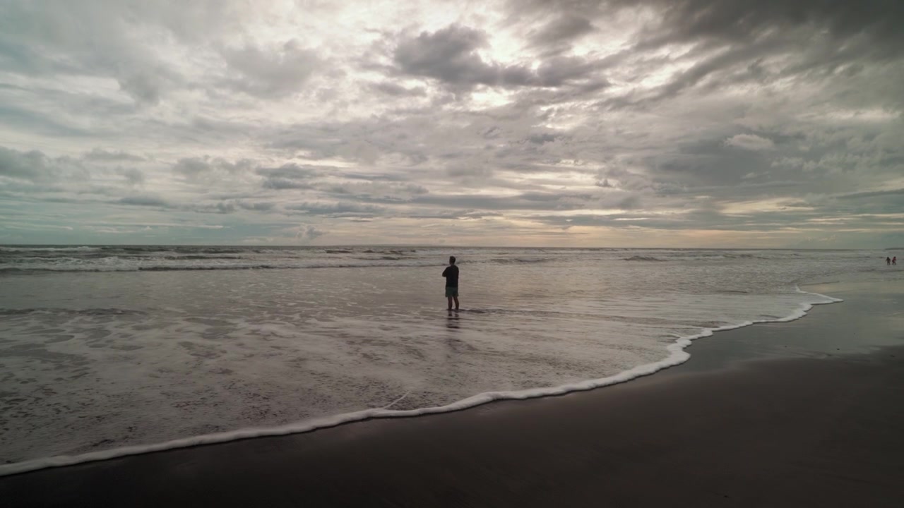 Persona in piedi da sola sulla spiaggia sotto un cielo nuvoloso