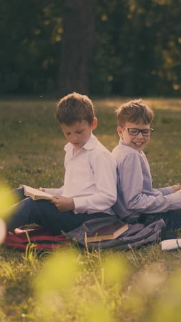 funny schoolmates in shirts prepare for exams together sitting on schoolbags in spring sunny park with shady places
