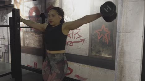 woman holds a gym rack and lifts a dumbbell sideways, stopping at shoulder height