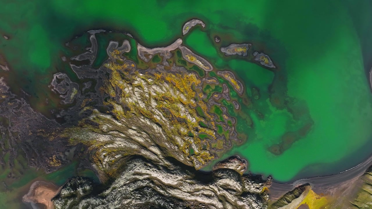 Aerial drone view of Landmannalaugar in Iceland with colorful rhyolite mountain lava field, and a turquoise green lake.