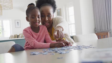 Happy-african-american-granddaughter-and-grandmother-doing-jigsaw-puzzle-at-home,-copy-space