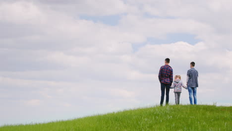 three children - two teenagers and a girl of 6 years standing on top of a green hill