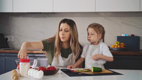 mom and young daughter sit in aprons in kitchen