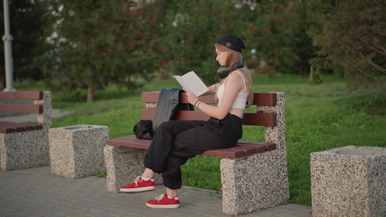 Donna immersa nella lettura di un libro all'aperto, studentessa concentrata nello studio in un parco soleggiato, giovane donna intenta a leggere materiale accademico seduta all'aperto in un parco soleggiato