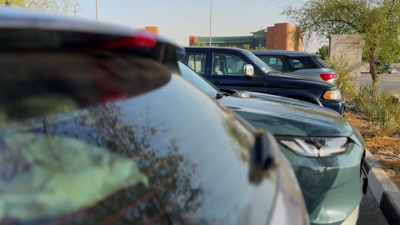 Cinematic 4K shot of cars parked in an outdoor urban lot with sunlight reflections and blurred city architecture in the background, perfect for transport, lifestyle, and city projects