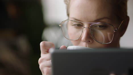 close-up-young-caucasian-business-woman-using-digital-tablet-computer-in-cafe-drinking-coffee-reading-email-messages-relaxing-watching-online-entertainment-on-portable-device-wearing-glasses