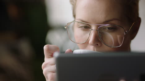 cerca joven mujer de negocios caucásica usando una tableta digital en un café bebiendo café leyendo mensajes de correo electrónico relajándose viendo entretenimiento en línea en un dispositivo portátil usando gafas