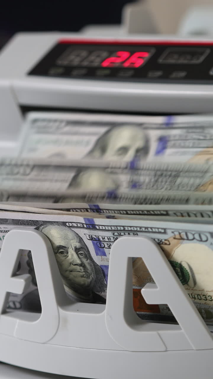 White compact cash counting machine working. One hundred dollar bills being turned in the counter. Close up. Vertical video