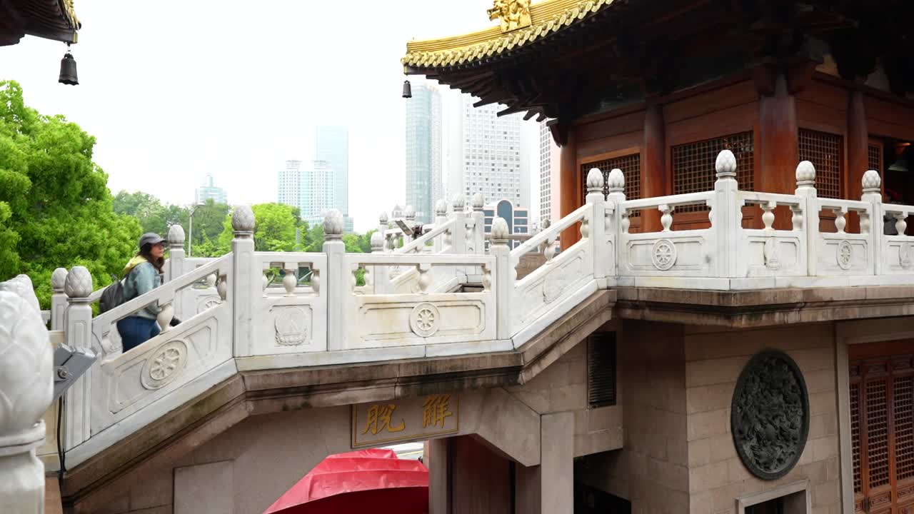 Caucasian tourist woman climbs stairs at Jingan Temple with modern skyscrapers in background, Shanghai, China