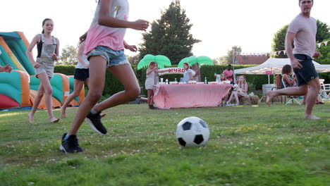 slow motion shot of children playing football match with adults at summer garden fete