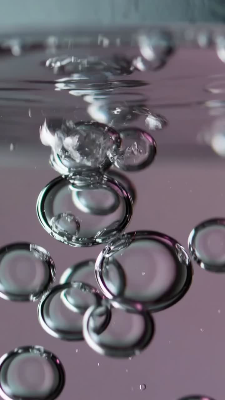Vídeo vertical: burbujas de aire ascendentes que se fusionan hacia arriba desde ondulaciones superficiales en un tanque con brillo azul verdoso