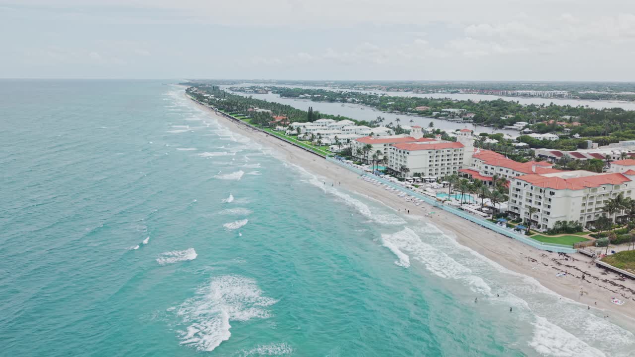 Dolly in drone shot of beach and hotels next to Atlantic Ocean with cloudy weather during the day in West Palm Beach, Florida, USA