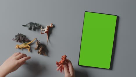 fotografía aérea de un niño jugando con dinosaurios de juguete junto a una tableta digital de pantalla verde