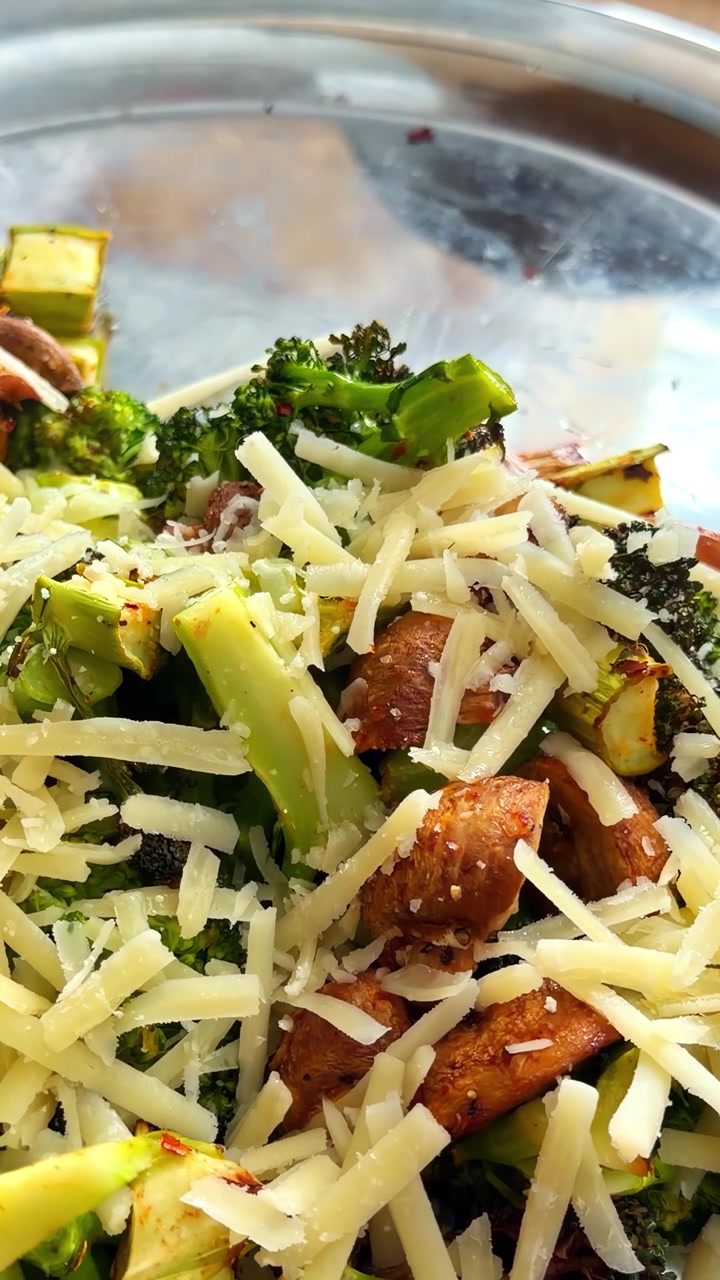 Broccoli, zucchine e funghi arrostiti, ricoperti di formaggio grattugiato in una ciotola di metallo, pronti per essere mescolati o serviti