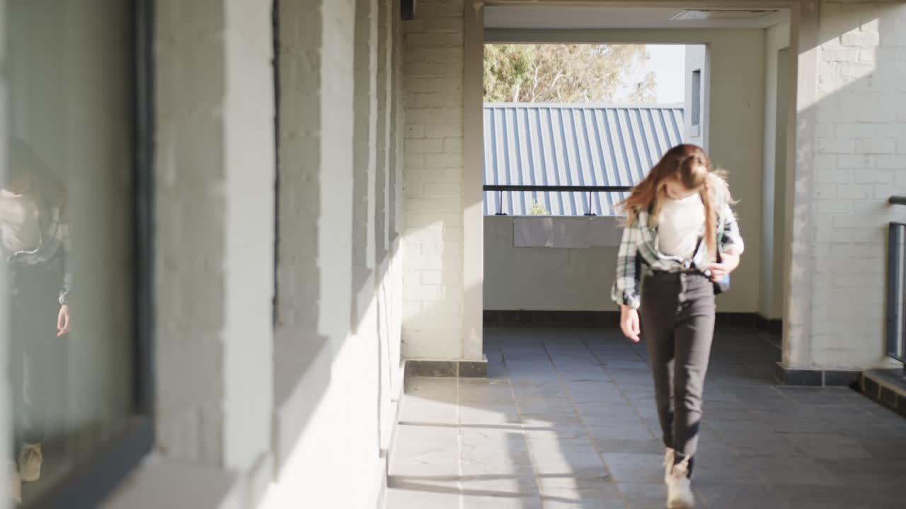 Young girl walking in school hallway, adjusting backpack, focused on task, copy space