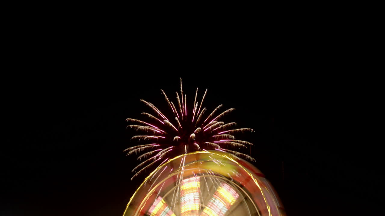 los fuegos artificiales explotan sobre una rueda de la fortuna en un lapso de tiempo