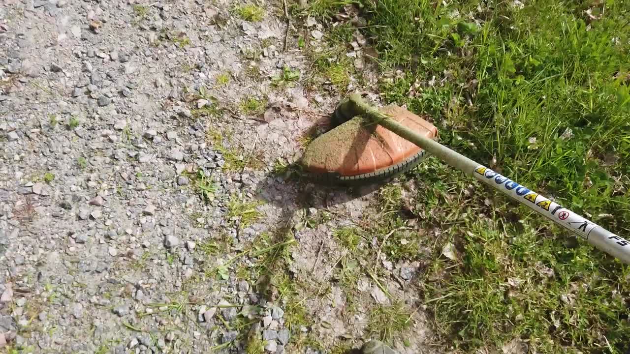 Overhead view of weed eater head by stony path cutting green grass in countryside, above pan
