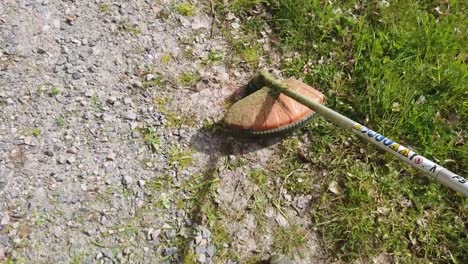overhead view of weed eater head by stony path cutting green grass in countryside, above pan
