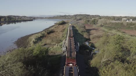 tonnes of railroad track hauled by train beside river suir, ireland