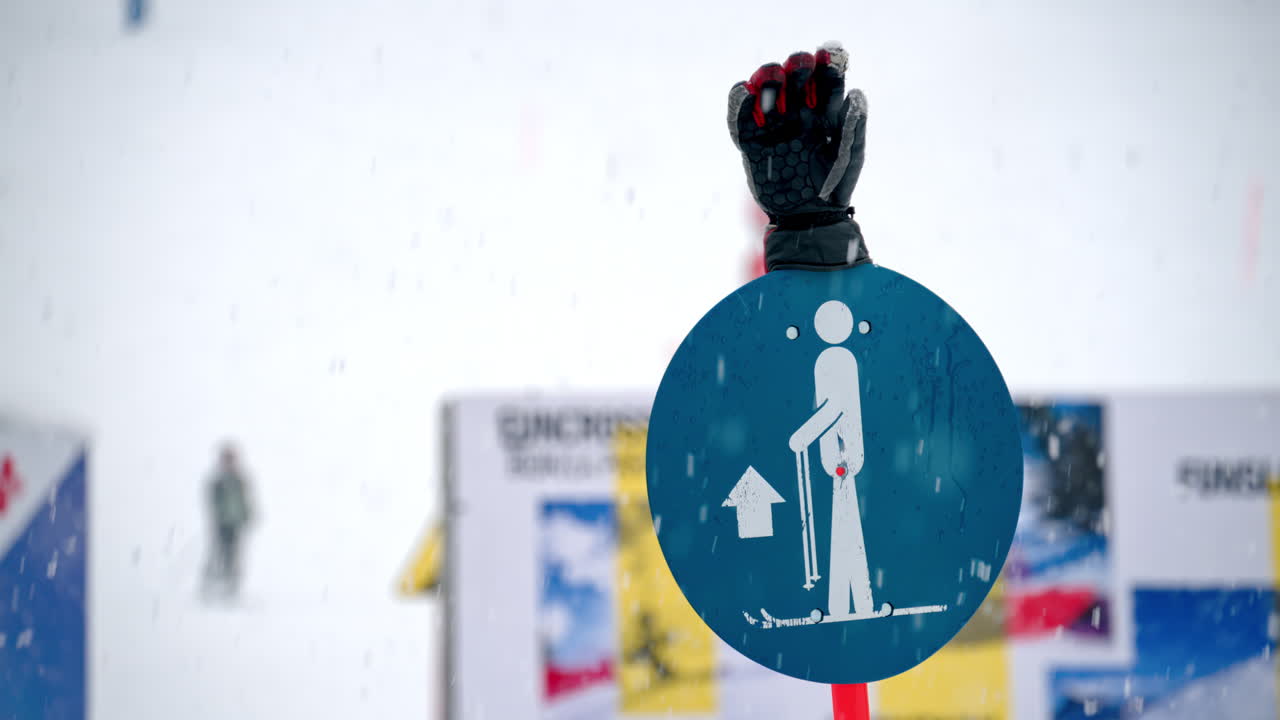 Close up of a ski sign with a ski glove on top in the snow with people skiing on the background