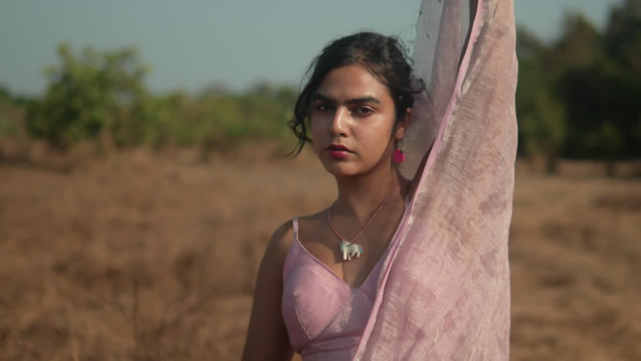 Donna in sari rosa che contempla in un campo secco, luce naturale calda