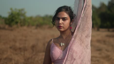 Mujer-Con-Sari-Rosa-Contemplando-En-Un-Campo-Seco,-Cálida-Luz-Natural.