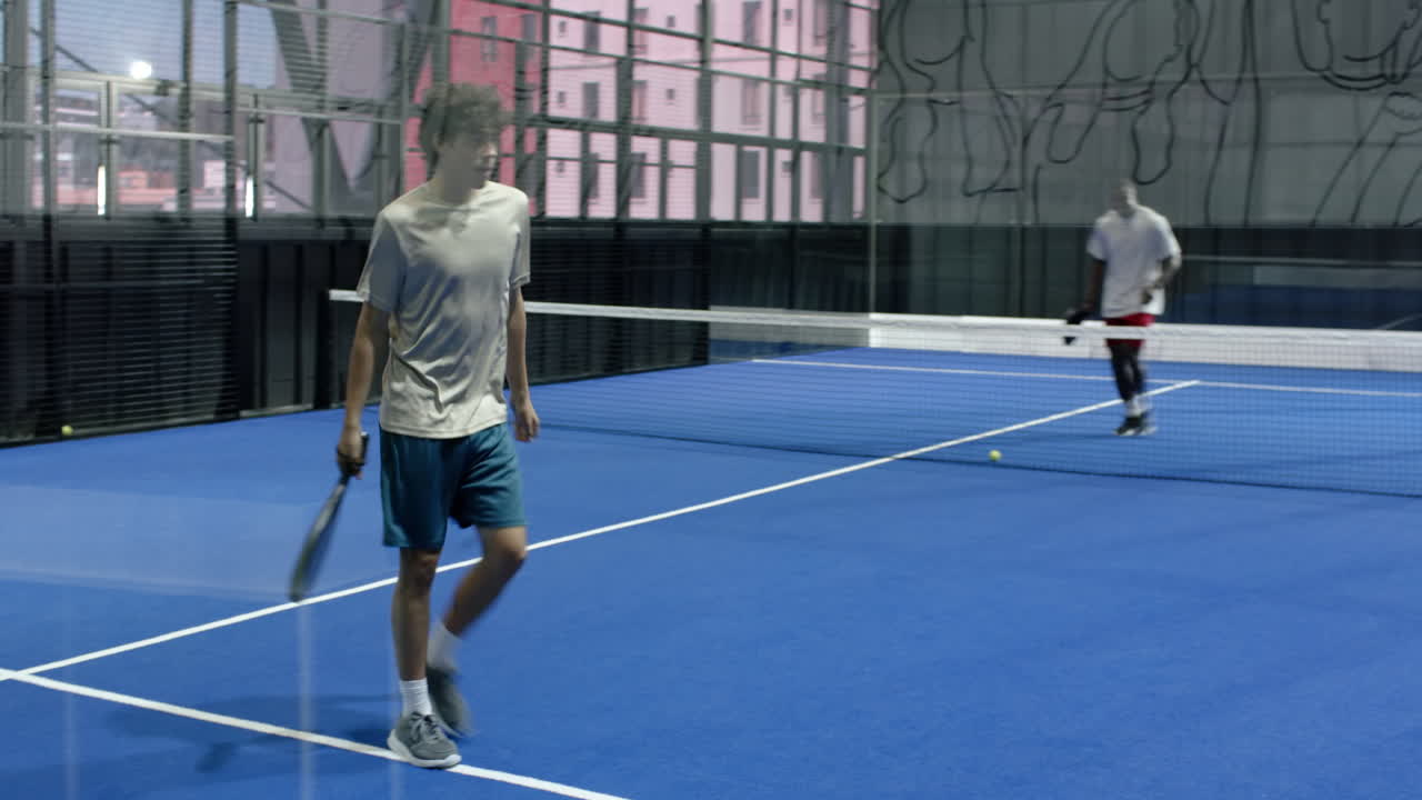 Young man playing padel tennis on indoor court, focusing on ball