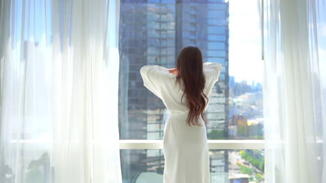 호텔 방에서 일어나 커튼을 열고 서있는 동안 팔을 뻗는 여자