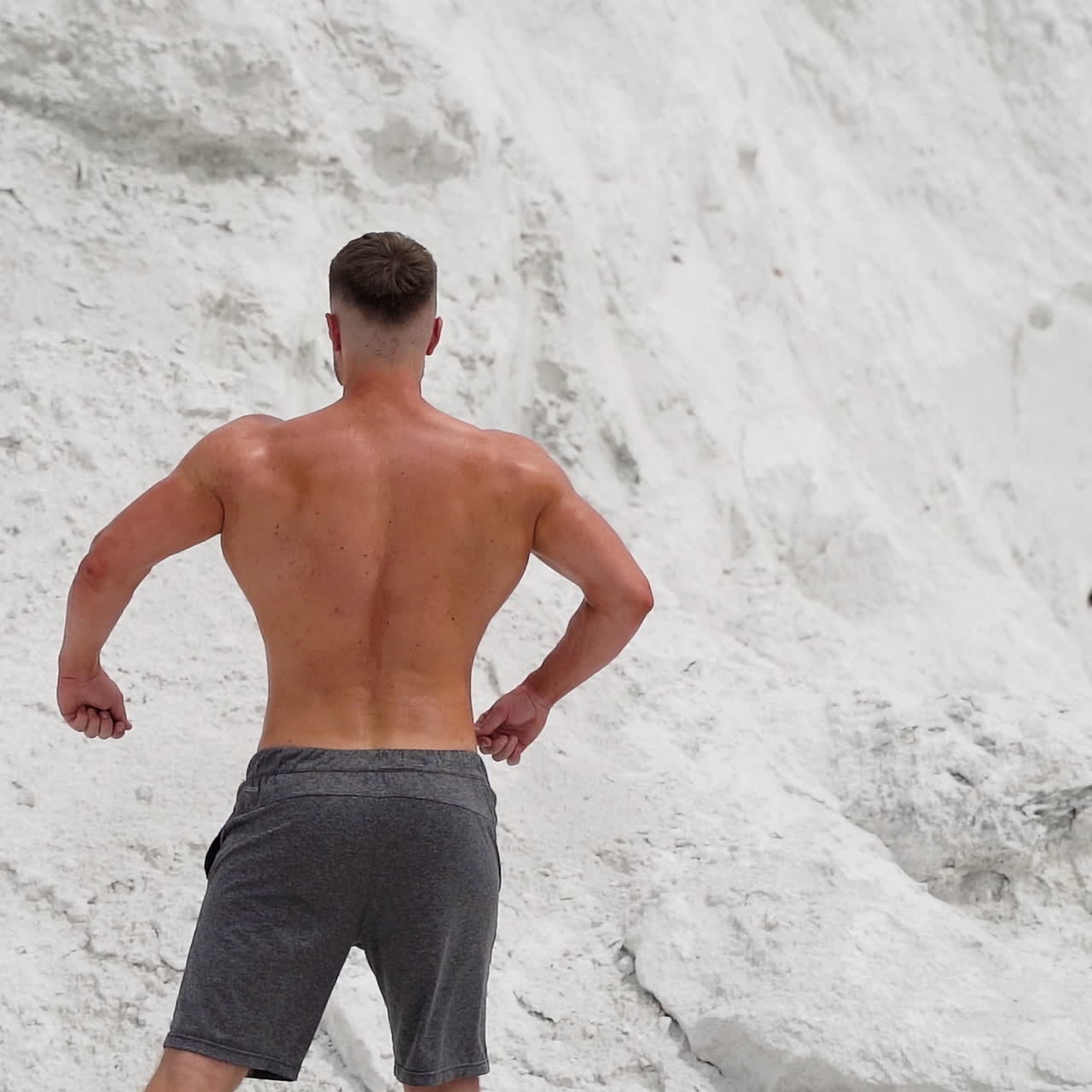 Back view of athlete with muscular body outdoors. Healthy body of a bodybuilder on white mountain background.