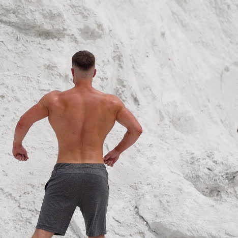back view of athlete with muscular body outdoors. healthy body of a bodybuilder on white mountain background.