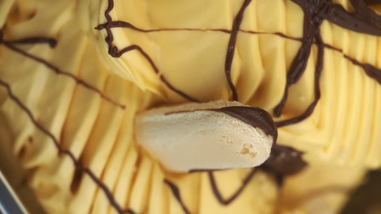Close-up of yellow ice cream with chocolate drizzle and a biscuit