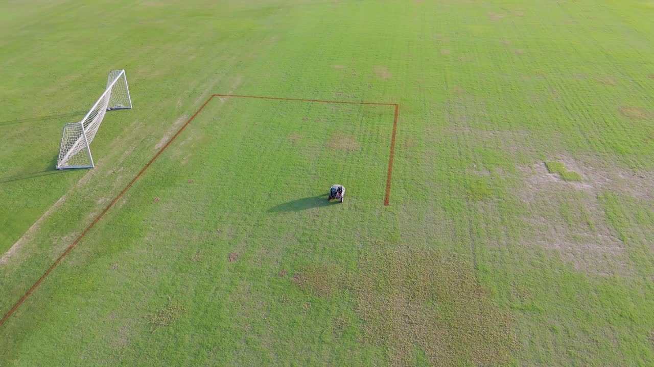 Aerial view of a robot autonomously painting precise lines on a soccer field under clear daylight