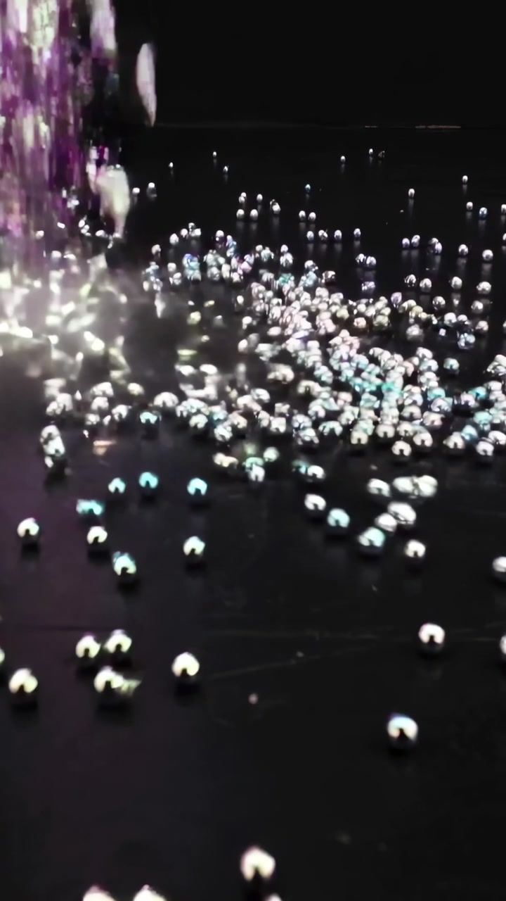 Vertical video: Starting bead column dropping onto dark glossy floor, creating cyan highlights