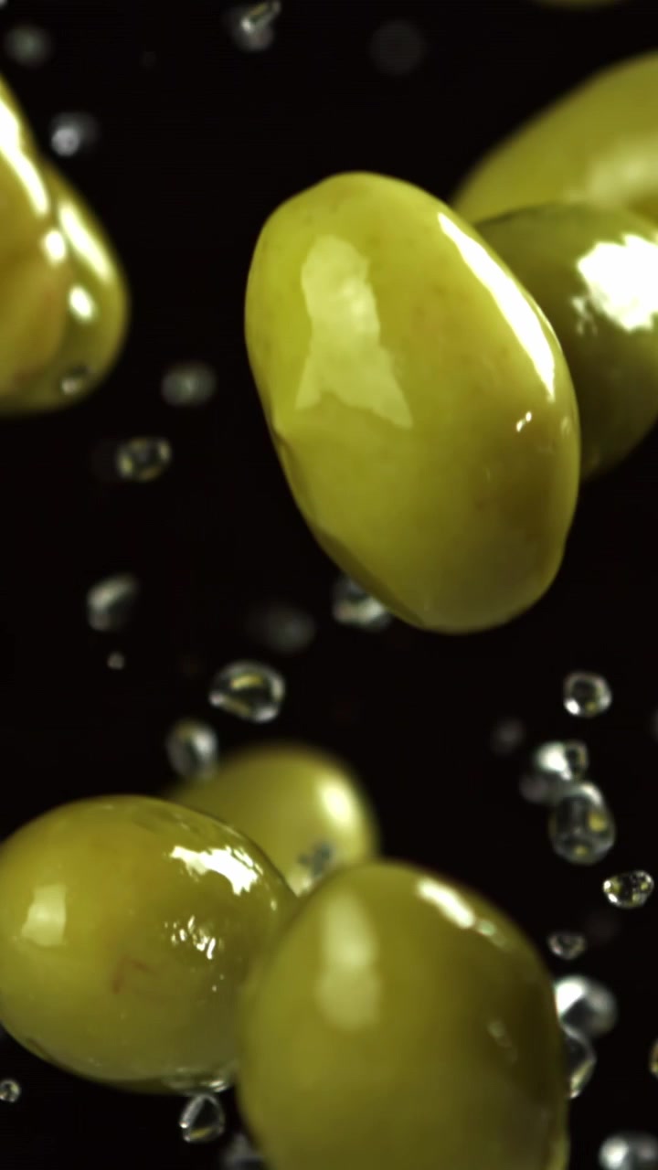 Olive verdi fresche che cadono con schizzi d'acqua su sfondo nero