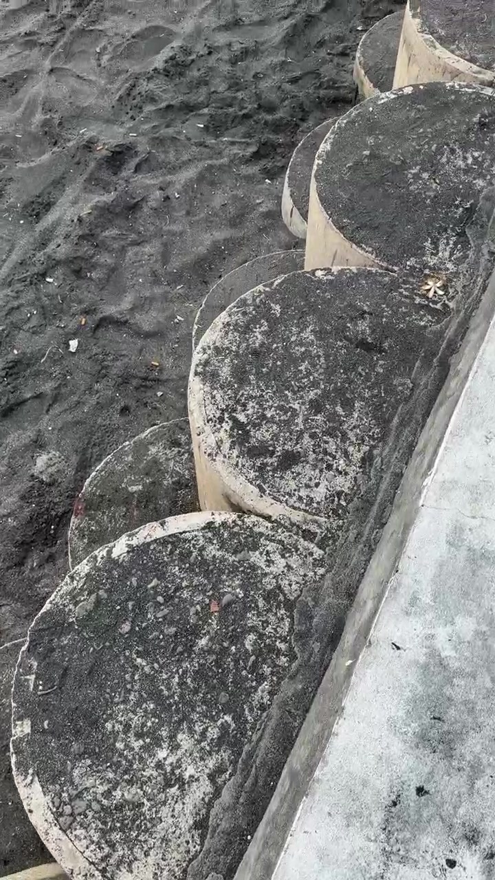 Person går ned ad betontrapper til sort sandstrand