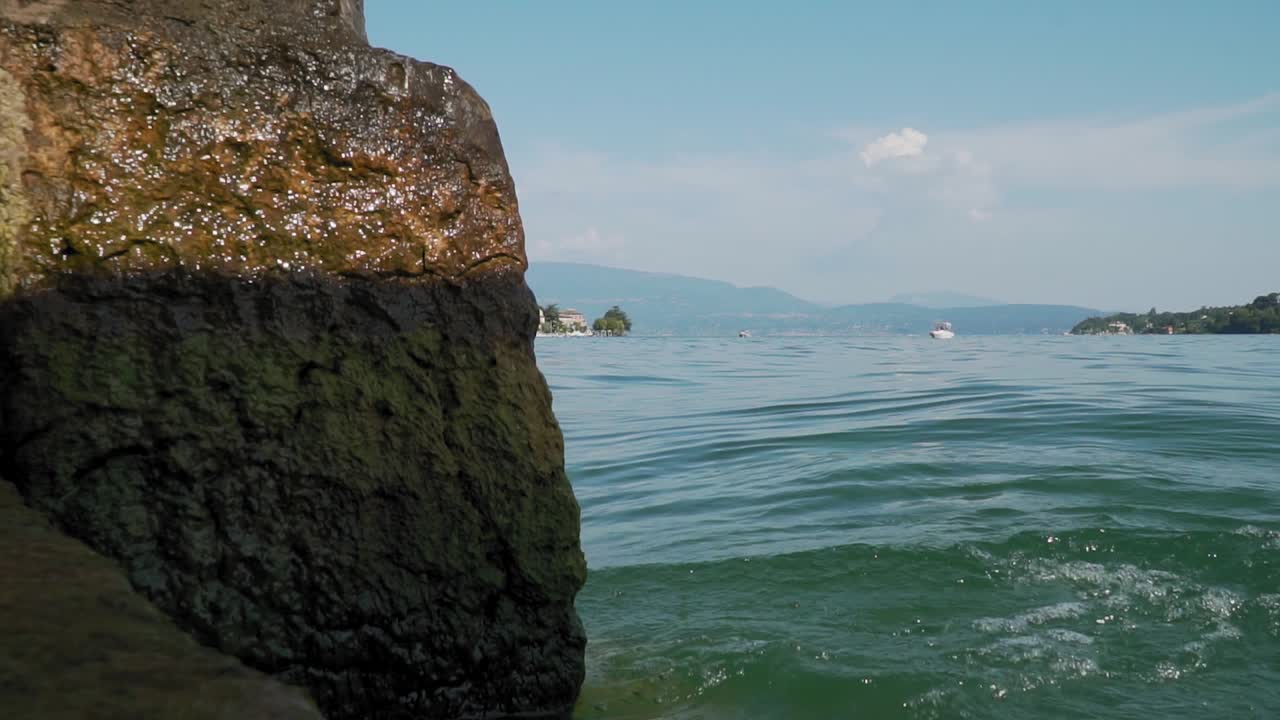 брызги воды на выветренной скале на берегу озера, вид на озеро на заднем плане