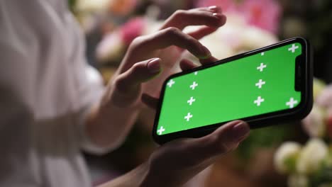 girl holds iphone smartphone in hands with green mockup chroma key screen for ad