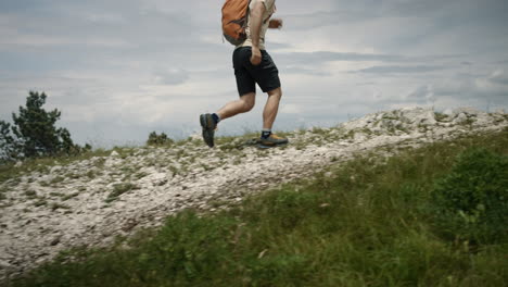 Camera-tracking-hiker-running-on-a-rocky-path-uphill-towards-the-concrete-monument-from-the-side,-towards-the-concrete-monument-on-top-of-mountain-Slavnik