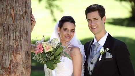 Happy-newlyweds-standing-in-the-park-beside-a-tree