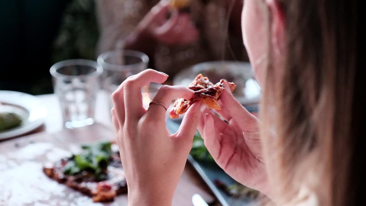 Woman biting into a pizza slice at a table with other people eating in the background