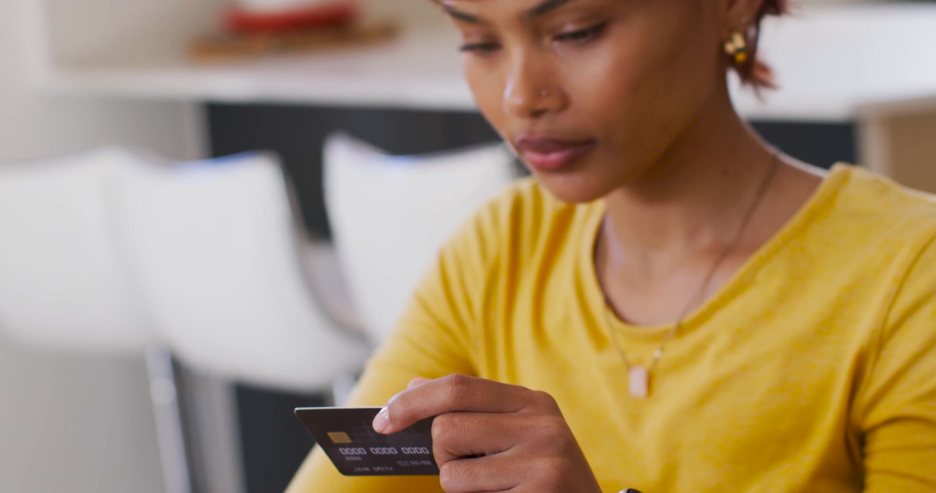 African woman grabbing credit card, rotating chip and checking laptop for payment at kitchen table