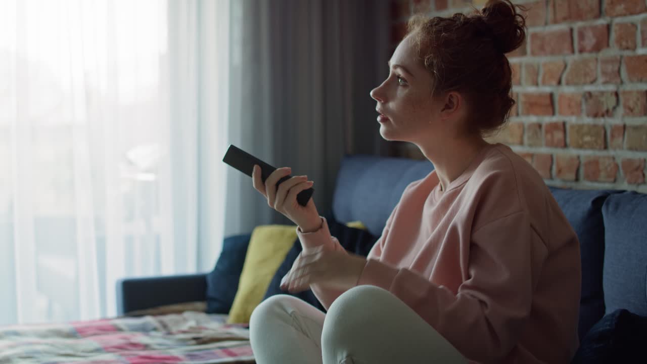 Vista laterale di giovane donna caucasica che guarda la TV a casa