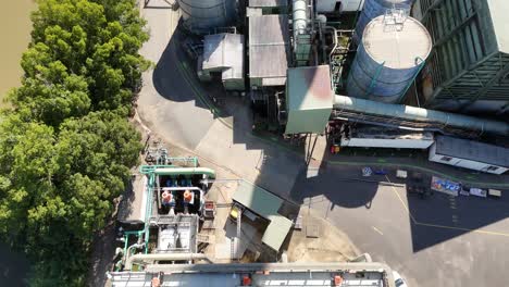 aerial footage of a sugarcane factory with cooling towers, adjacent river, and rural landscape under clear skies