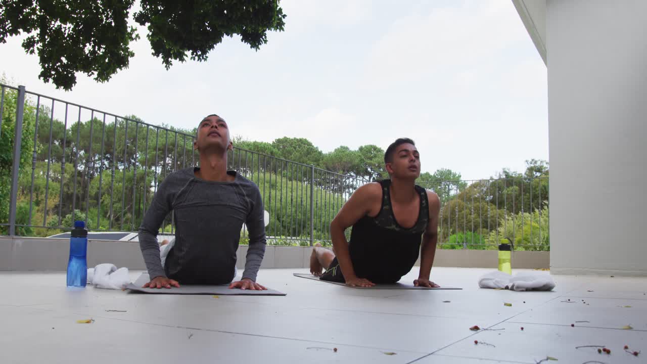 pareja de hombres homosexuales de raza mixta de pie en la terraza practicando yoga