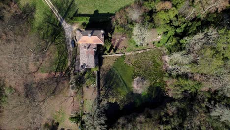 aerial-view-with-drone-approaching-a-large-wooded-lot-with-view-on-the-roof-of-an-old-house,-large-lot-and-variety-of-trees,-small-dirt-road