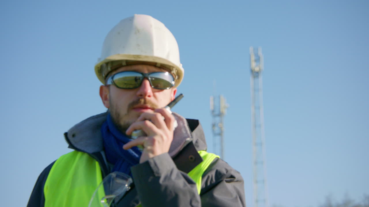 ingeniero masculino hablando por radio con torres celulares en el fondo mientras cambia el enfoque del sujeto, primer plano