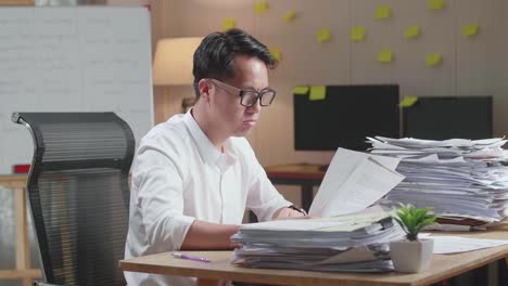 tired asian man yawning while working hard with documents at the office